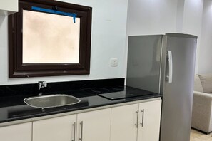 Cozinha com bancada preta, pia de aço inoxidável, armários brancos e geladeira prateada.