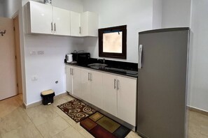 A compact kitchen with white cabinets, a stainless steel sink, a black countertop, and a refrigerator. - Chalet with side sea and pool view, Turtles Beach (Hurghada 2)