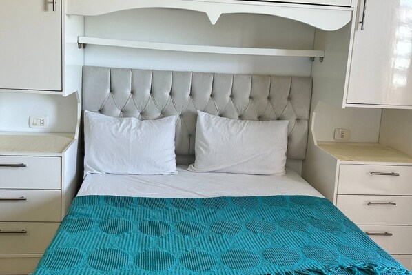 Uma cama com cabeceira estofada, duas almofadas brancas e um cobertor verde-água.