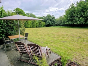 Eine Terrasse im Freien mit Tisch und Stühlen, einem großen Sonnenschirm und einem Rasen.