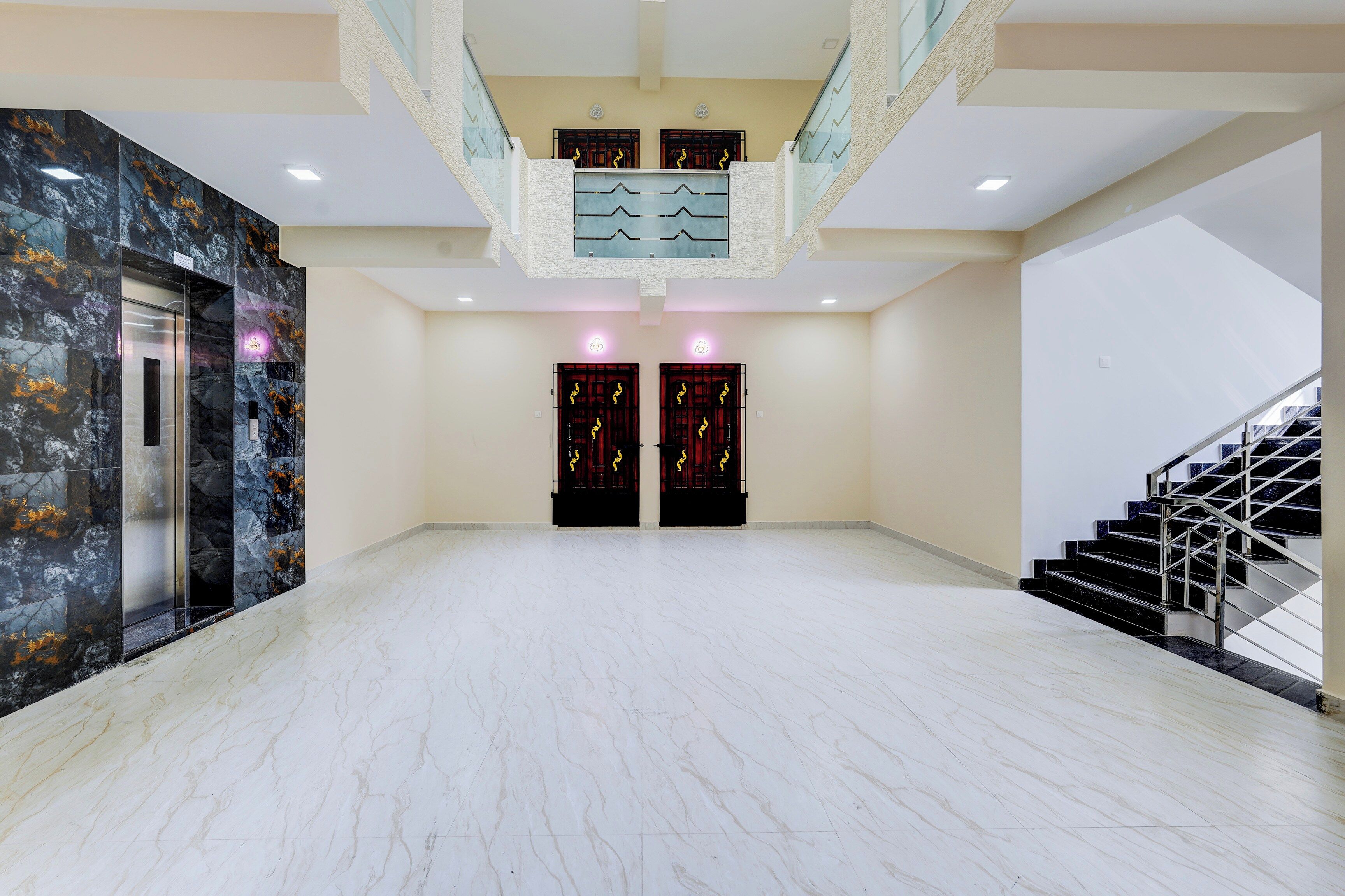 A spacious lobby with marble flooring, a staircase, and a modern elevator.