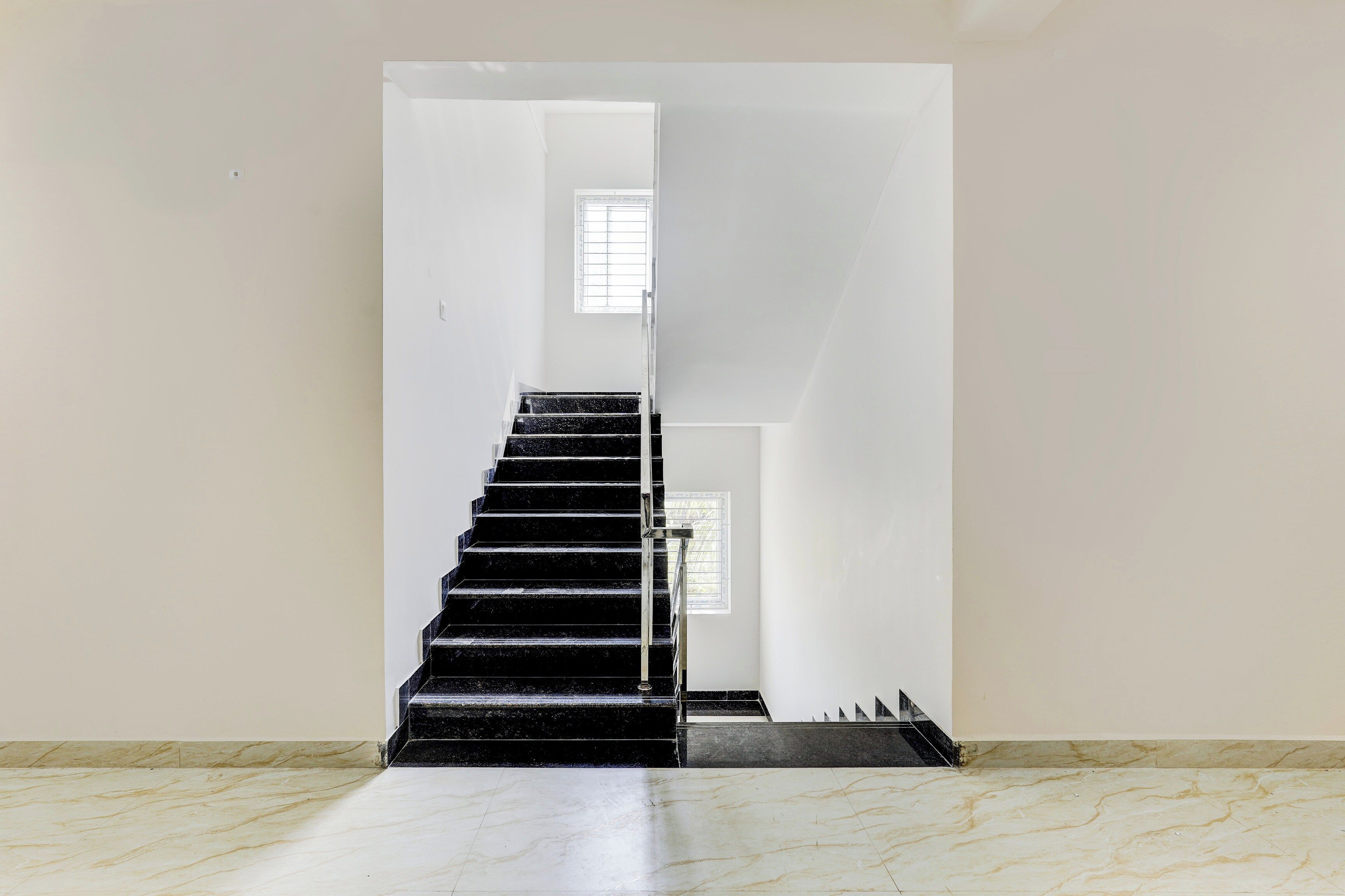 A staircase with a handrail leading to a landing, a window with blinds, and a marble floor.