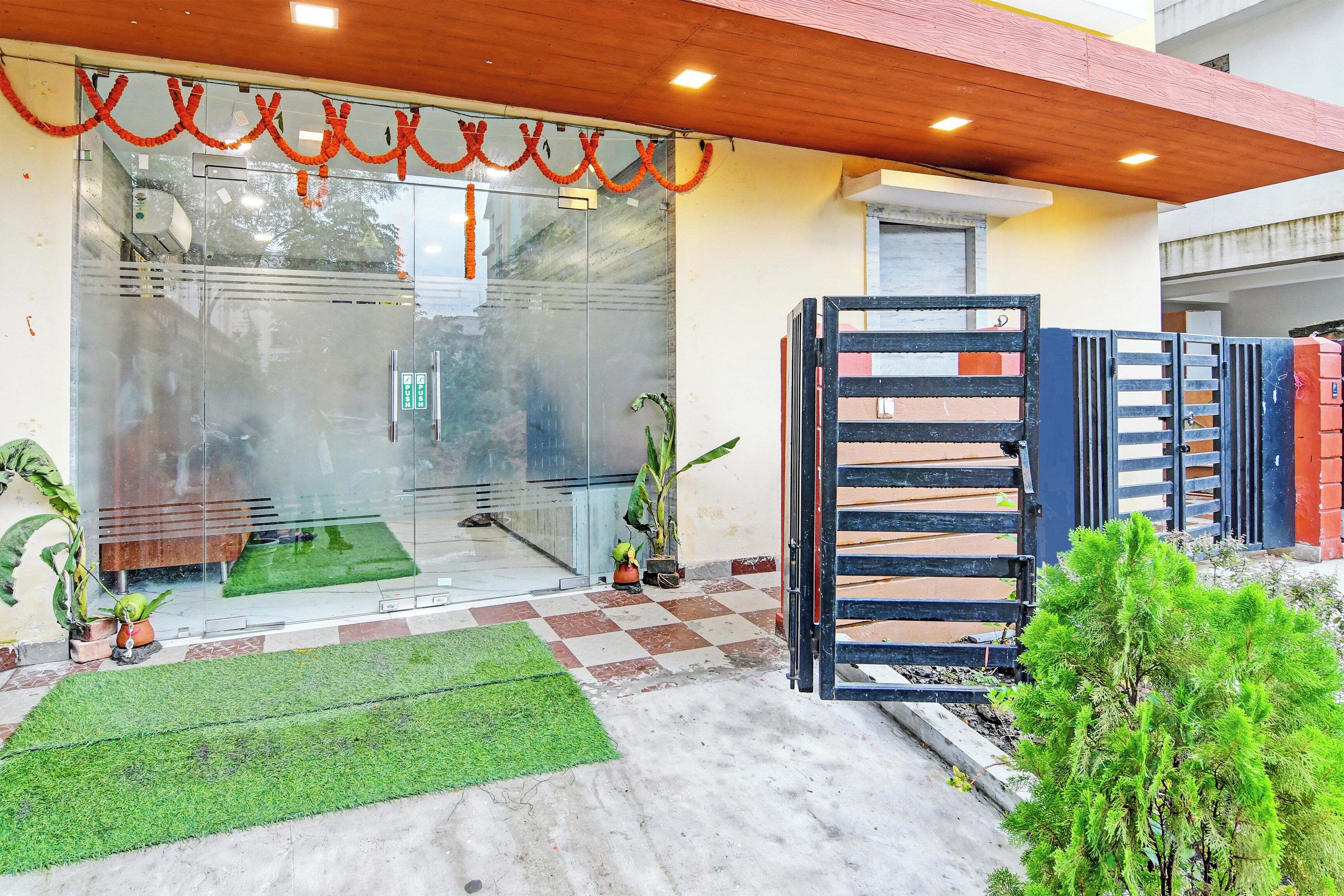 Entrada de un edificio con puerta de vidrio, piso a cuadros y un pequeño césped.