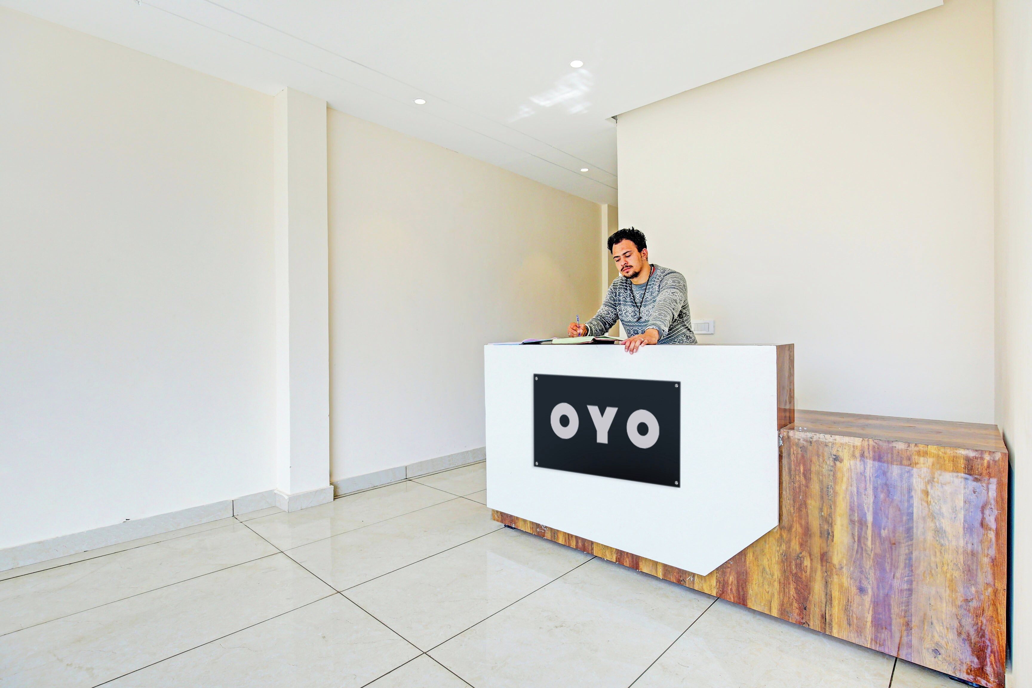 A reception desk with a sign that reads 'OYO' in a modern, minimalistic lobby with tiled flooring and plain walls.