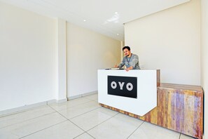 Un mostrador de recepción con un cartel que dice 'OYO' en un vestíbulo moderno y minimalista, con suelo de baldosas y paredes lisas.