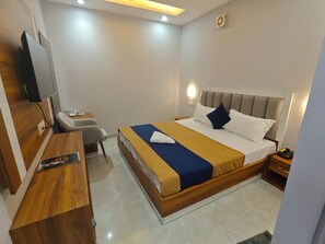 A hotel room with a bed, bedside table, chair, desk, and a television. - Live as LDH349 (Ludhiana)