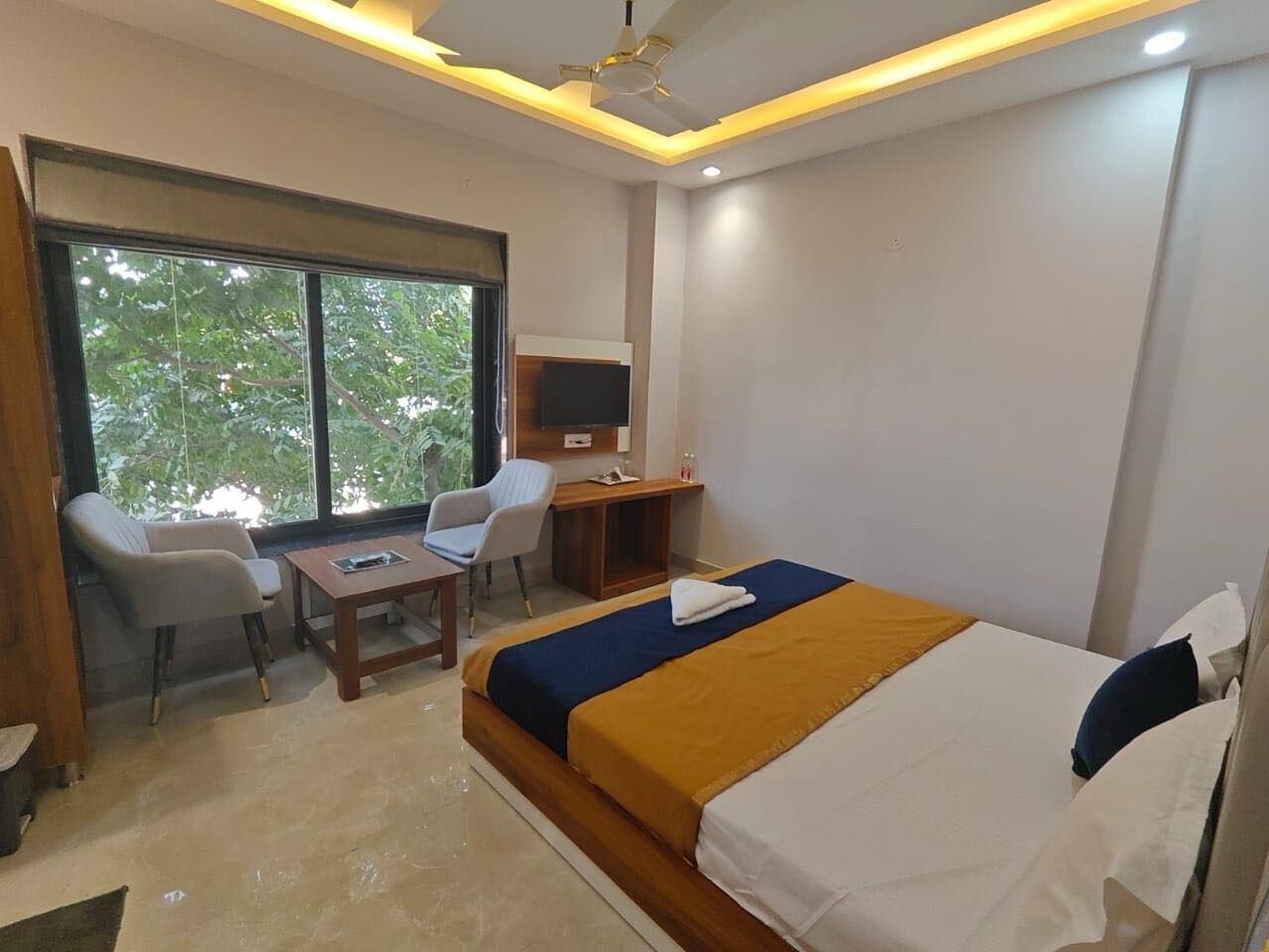 A hotel room with a bed, a desk, a chair, a TV, and a window with a view of trees.