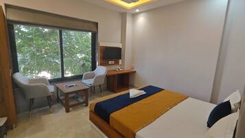 A hotel room with a bed, a desk, a chair, a TV, and a window with a view of trees.
