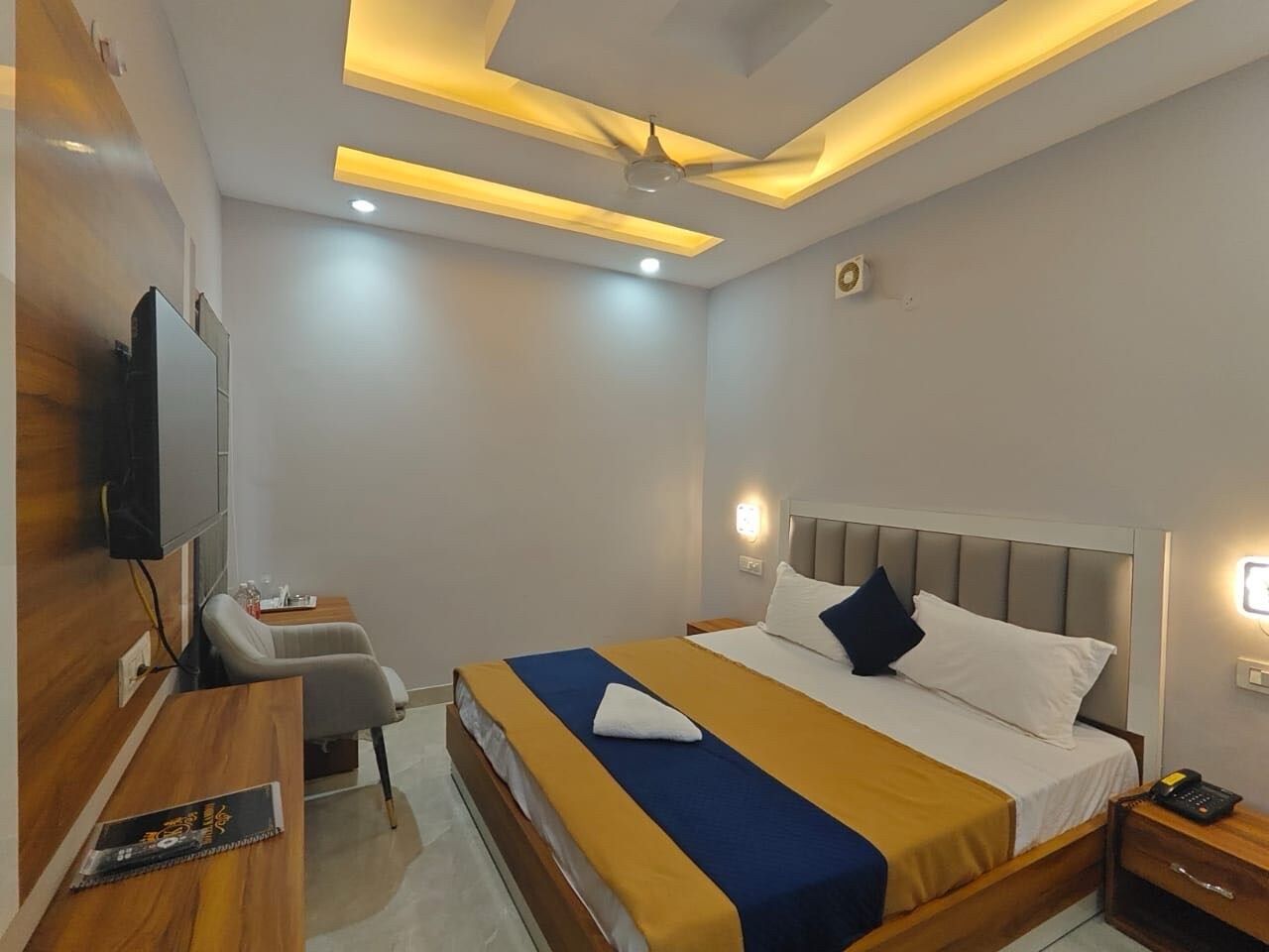 A modern hotel room with a bed, bedside table, and a flat-screen TV mounted on the wall.