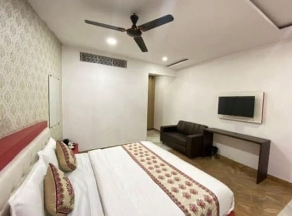 A hotel room with a bed, a ceiling fan, a TV mounted on the wall, and a sofa. - Live as LDH349 (Ludhiana)