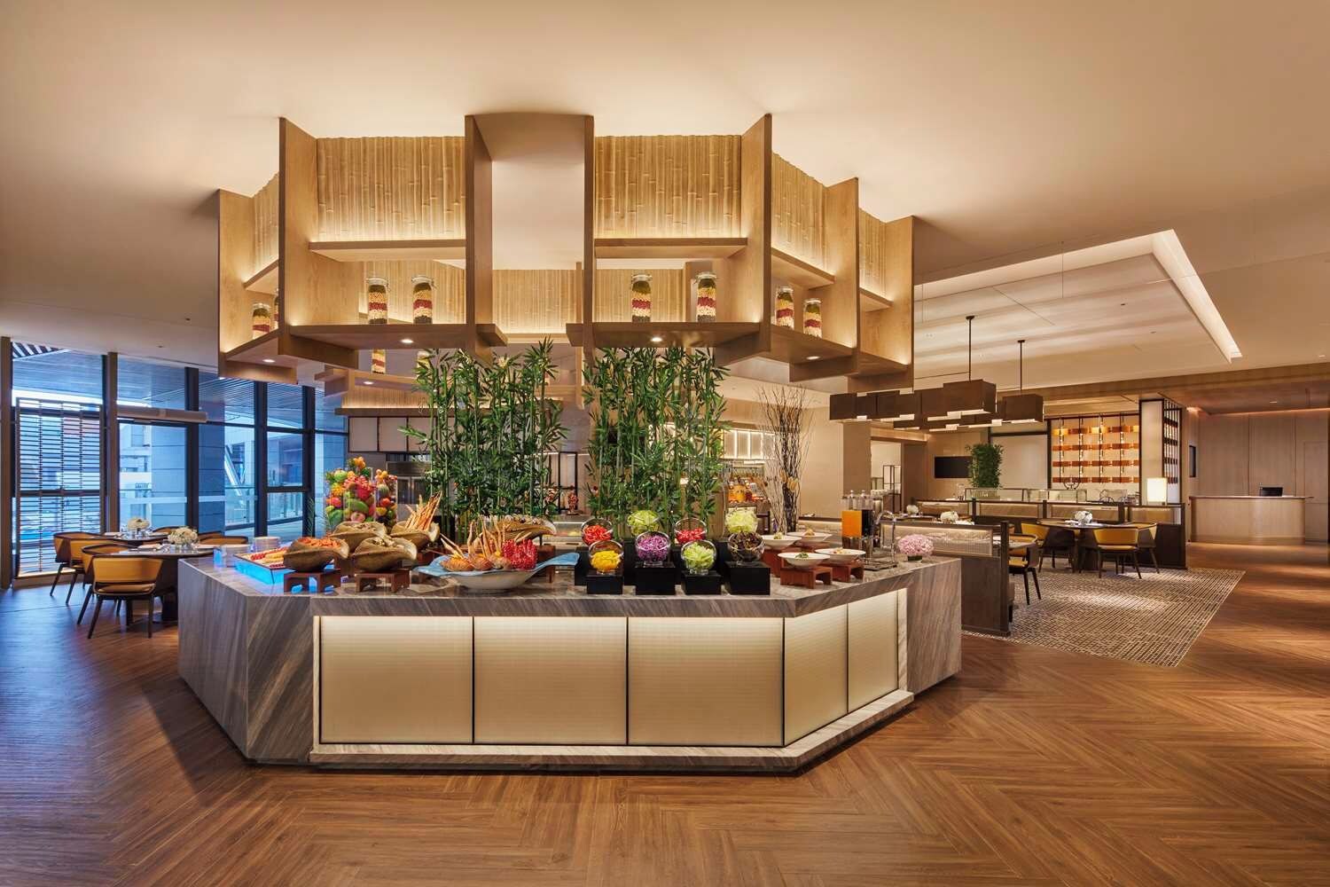 Un lobby moderno de hotel con una barra central, arreglos de asientos y un amplio ventanal con vistas.