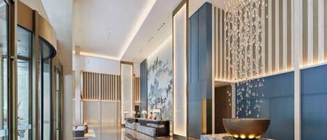 A modern lobby with a reception desk, a large decorative bowl, and a chandelier.