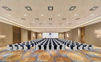 A conference room with rows of tables and chairs, a large screen at the front, and a patterned carpet.