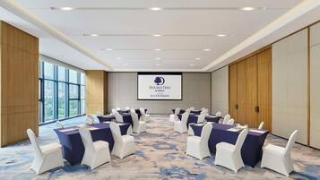 Ein Konferenzraum mit einer großen Leinwand, die das DoubleTree by Hilton Logo zeigt, weißen Stühlen und einem Teppichboden.