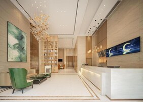 A modern hotel lobby with a reception desk, seating area, and a large wall-mounted artwork.