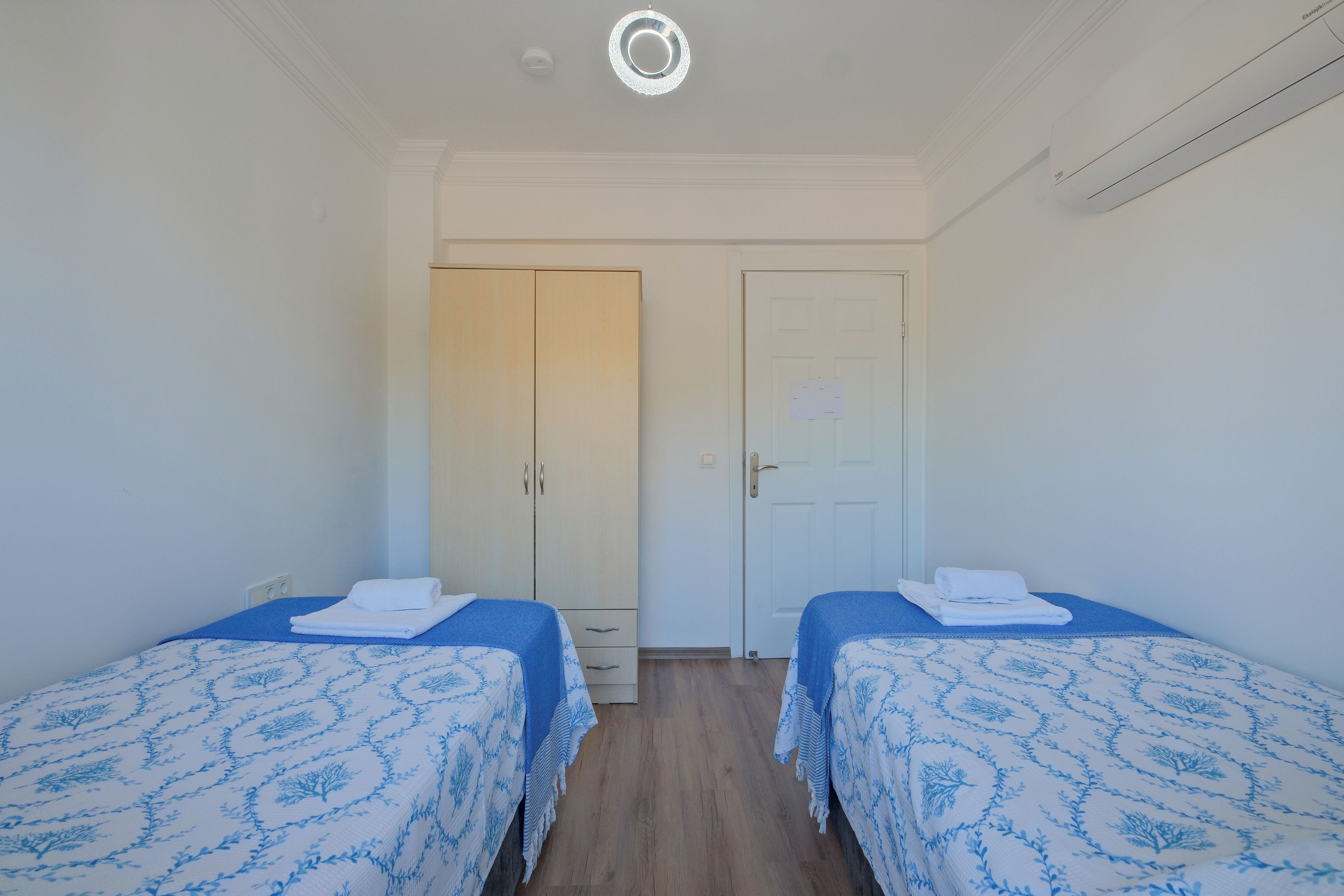 Una habitación con dos camas, cada una con colcha de diseño azul y blanco, un armario blanco y una puerta blanca con cerradura.