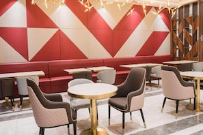 En modern restauranginteriör med röda och vita väggar i ett geometriskt mönster, bekväma sittplatser och runda bord med guldfärgade detaljer.