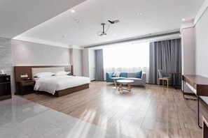 Ett modernt hotellrum med en stor säng, en soffa, ett litet runt bord och ett skrivbord.