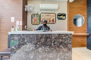 Un comptoir d’accueil avec un plateau en marbre, un climatiseur fixé au mur et des œuvres d’art religieuses encadrées.