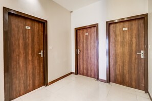 Trois portes en bois, portant les numéros 207, 206 et 205, se trouvent dans un couloir dont le sol est recouvert de carreaux blancs.