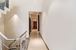 A hallway with a staircase on the left, a wooden door at the end, and a light fixture on the wall. - Hotel O City Inn (Amritsar)