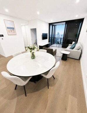 A modern living room with a round dining table, a sofa, and a TV. - Luxury 2BR | Ocean Views | Level 50 Broadbeach (Broadbeach)