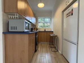 A compact kitchen with wooden cabinets, a microwave, a refrigerator, and a window providing natural light. - Cremorne Point Harbour Escape (Cremorne Point)