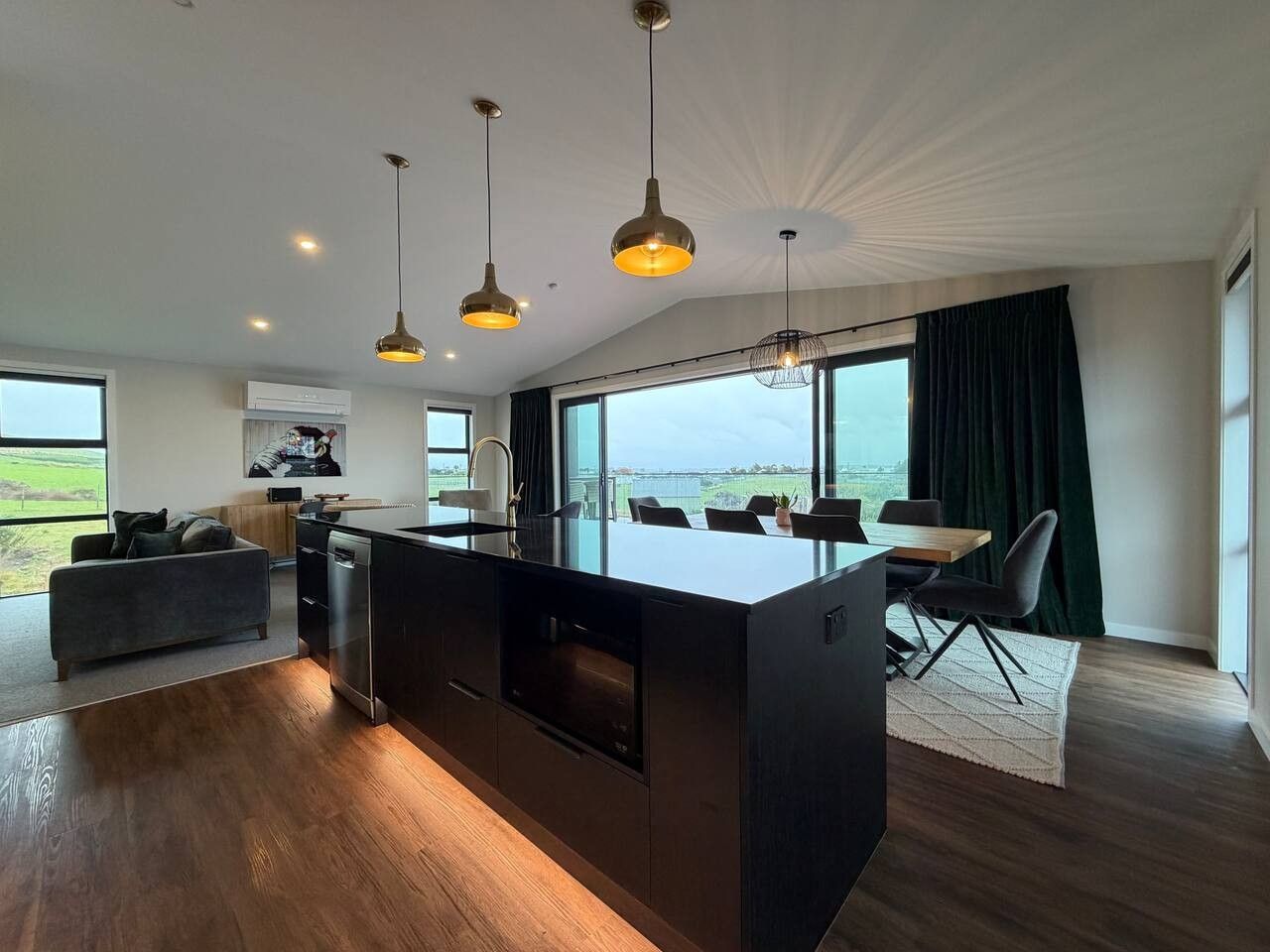 A modern kitchen with a central island, pendant lighting, and a dining area with a view.