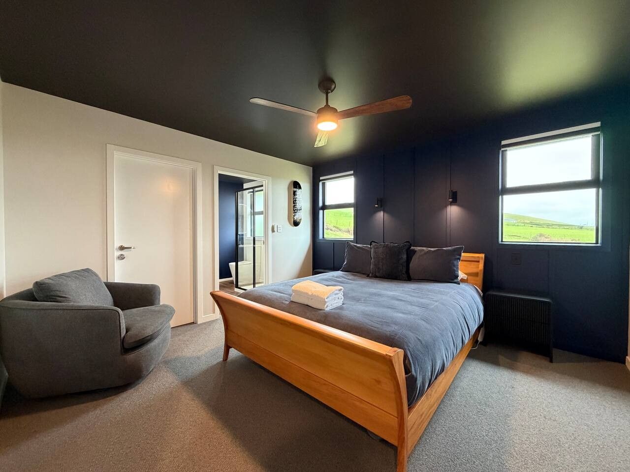 A bedroom with a bed, a chair, a ceiling fan, and a window.