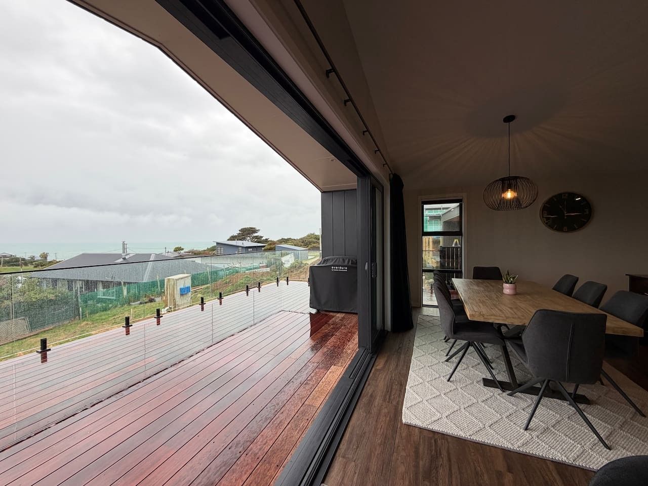 Ein modernes Interieur mit einem großen Holzbalkon, einem Essbereich mit Tisch und Stühlen und Blick auf die umliegende Landschaft.