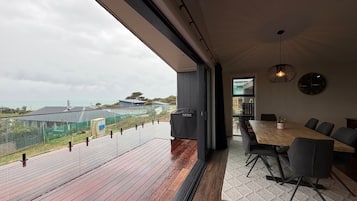 Ein modernes Interieur mit einem großen Holzbalkon, einem Essbereich mit Tisch und Stühlen und Blick auf die umliegende Landschaft.
