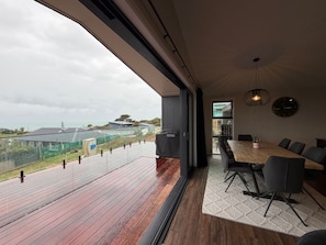 A modern interior with a large wooden deck, a dining area with a table and chairs, and a view of the surrounding landscape. - Luxe Lookout Riverton (Riverton / Aparima)