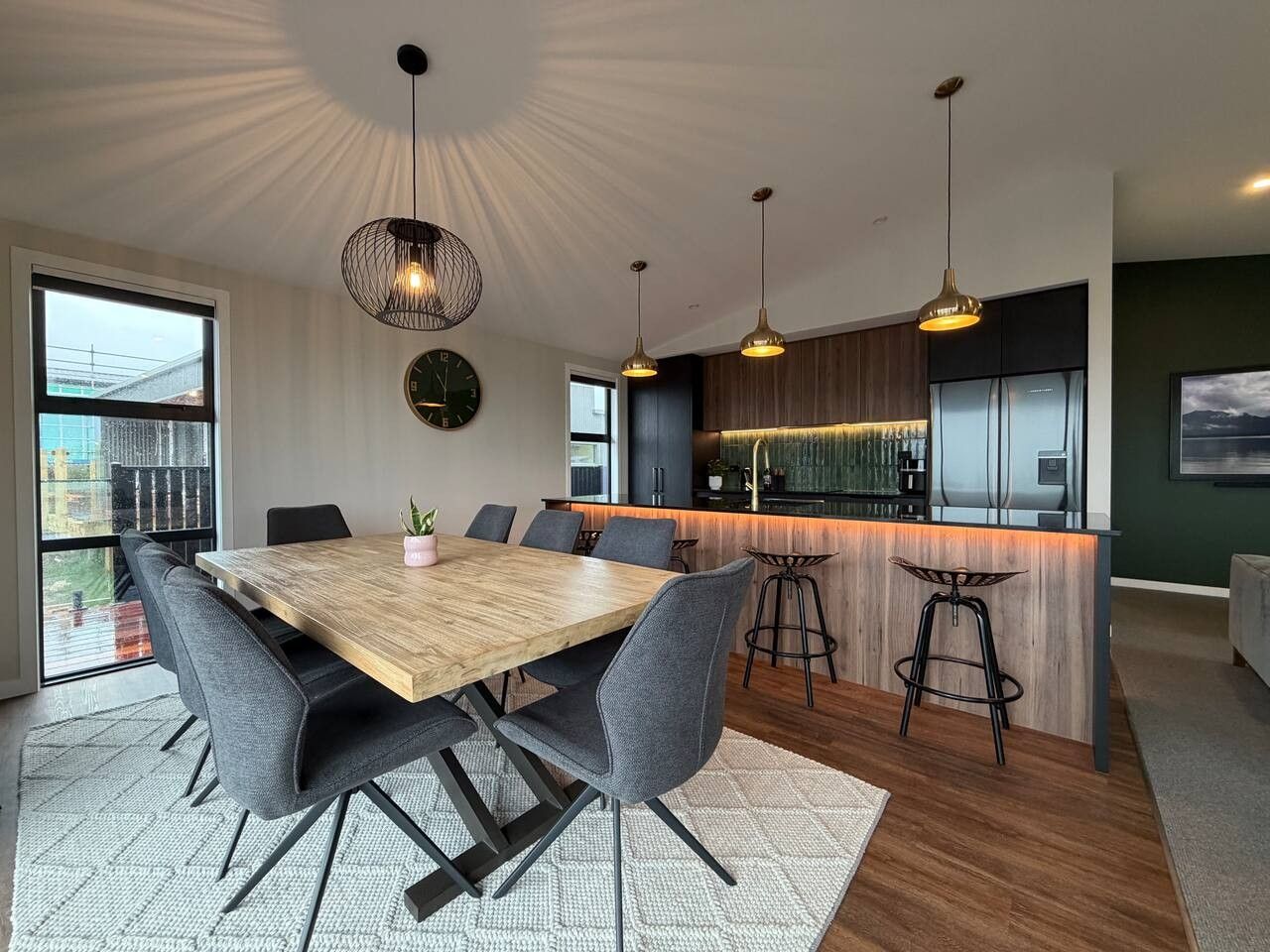 Eine moderne Küche mit einer Holztheke, Barhocker, Pendelleuchten und Blick auf die Stadt durch große Fenster.