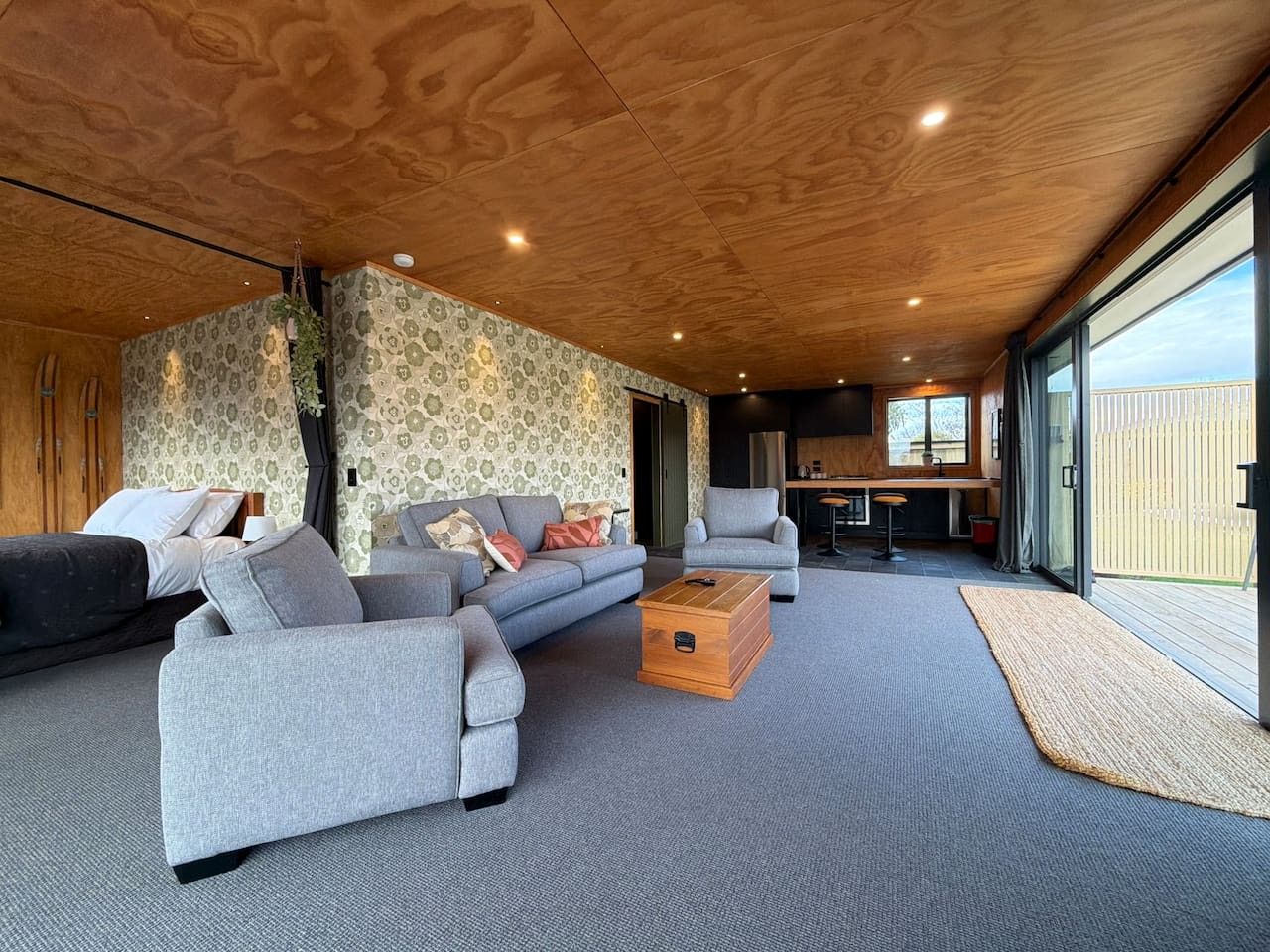 Un salon moderne avec un canapé d’angle gris, une table basse en bois et une grande fenêtre donnant sur l’extérieur.