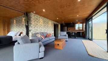 Un salon moderne avec un canapé d’angle gris, une table basse en bois et une grande fenêtre donnant sur l’extérieur.