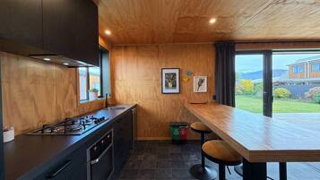 Une cuisine moderne avec un plafond en bois, une cuisinière à gaz, des meubles de rangement aux couleurs sombres et une grande fenêtre donnant sur un jardin.