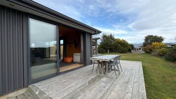 Une maison moderne dotée d’une terrasse, d’une porte-fenêtre coulissante donnant sur l’intérieur et offrant une vue sur le paysage environnant.