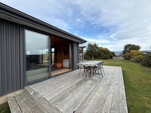 Ein modernes Haus mit einer Terrasse, einer Schiebetür zu einem Innenbereich und Blick auf die umliegende Landschaft.