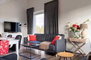 A modern living room with a sofa, coffee table, and a dining area with a table and chairs. - Levi North Apartment D11 by Aavalevi (Levi)