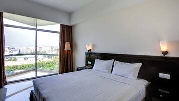 Habitació d'hotel amb un llit gran, dues làmpades de nit, una tauleta de nit i vista a un paisatge urbà a través de finestres de sostració a terra.