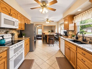 A kitchen with wooden cabinets, a stainless steel refrigerator, a microwave, a stove, and a ceiling fan. - Overland Park Retreat with Pool & Shuffleboard! (Overland Park)