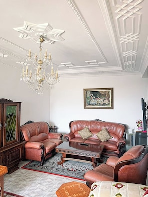 A living room with leather sofas, a chandelier, a painting, and a traditional rug. - Charming Tangier Apartment Central, Iconic, and Comfortable (Tanger)