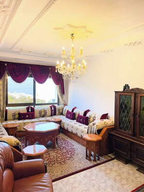 A spacious living room with a large sofa set, a wooden coffee table, and a chandelier. - Charming Tangier Apartment Central, Iconic, and Comfortable (Tanger)