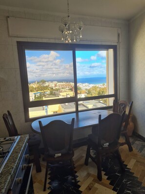 A room with a large window, a dining table, chairs, and a chandelier. - Charming Tangier Apartment Central, Iconic, and Comfortable (Tanger)