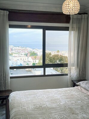 A bedroom with a large window, a bed, and a chandelier. - Charming Tangier Apartment Central, Iconic, and Comfortable (Tanger)