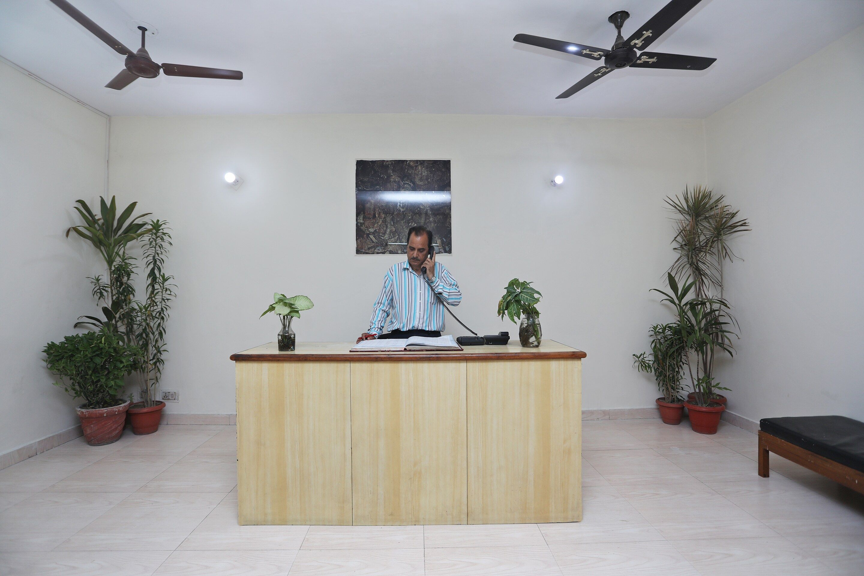 A reception desk with a man standing behind it, two ceiling fans, and potted plants on either side.