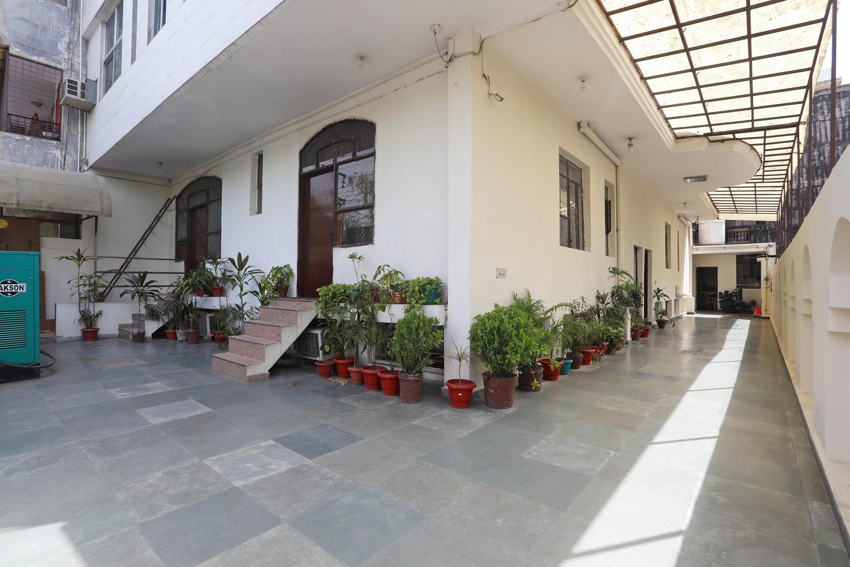 A covered outdoor area with potted plants, a staircase, and a building with multiple windows.