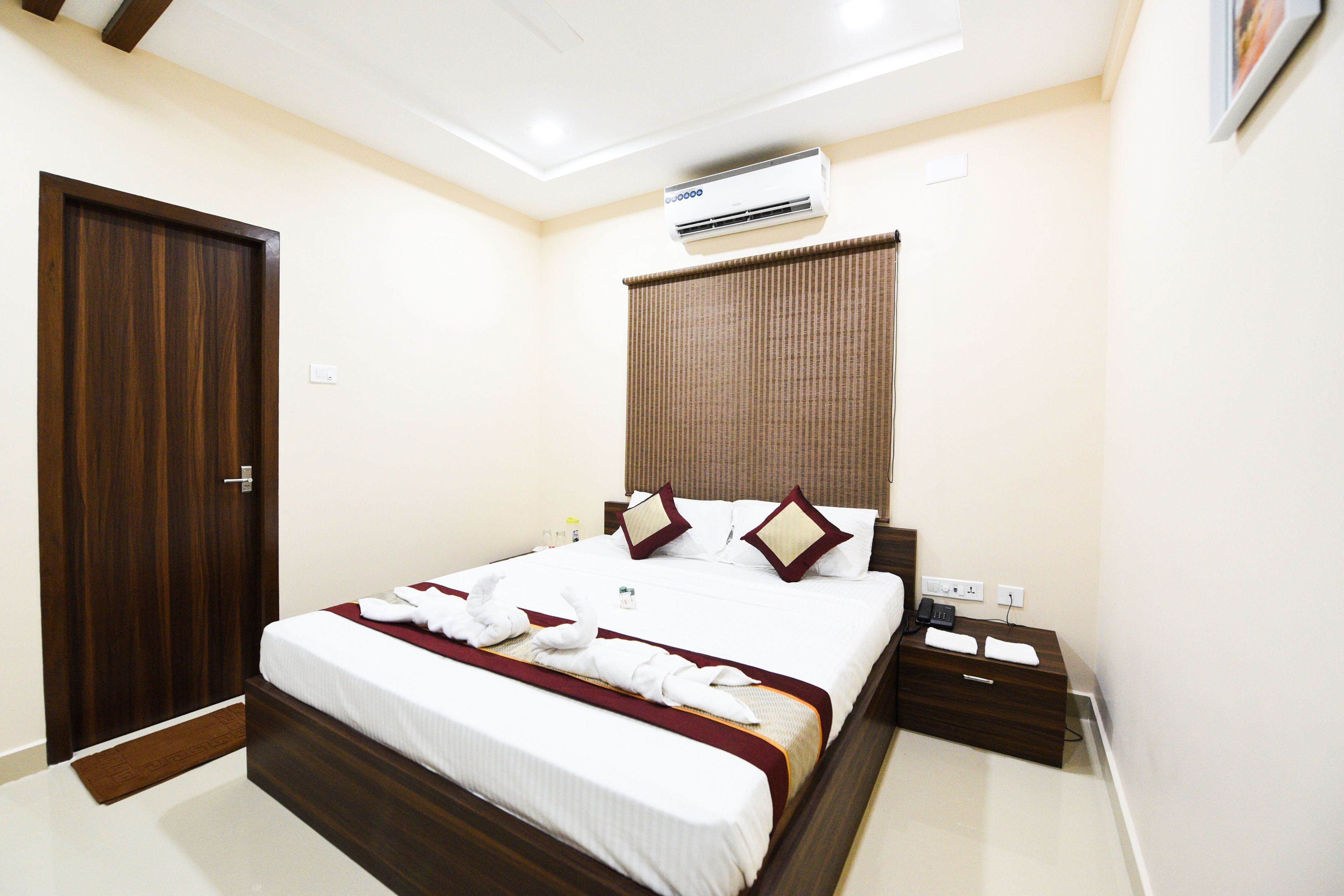 A hotel room with a bed, bedside table, and an air conditioning unit.