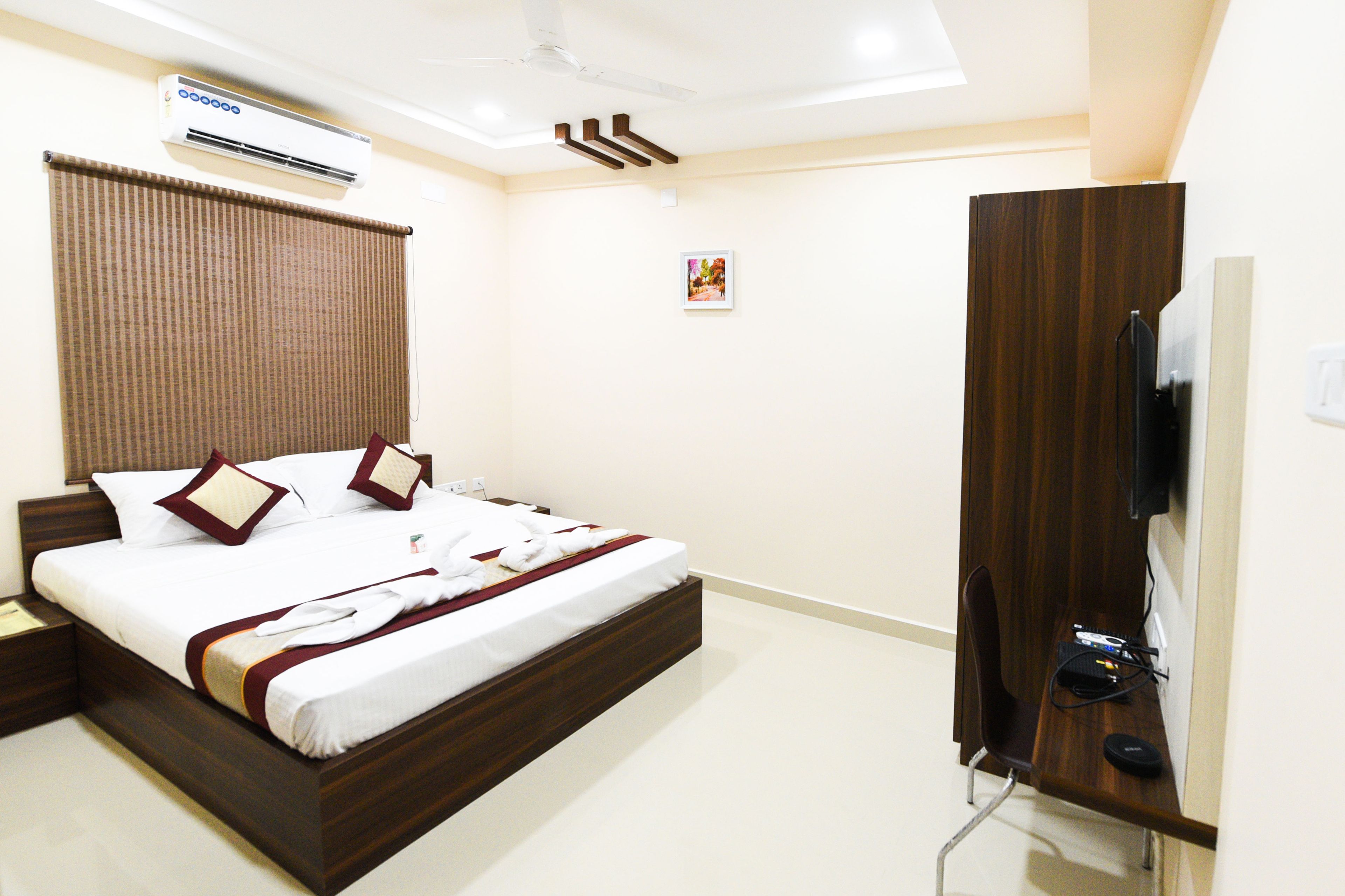 A hotel room with a bed, a television, and an air conditioning unit.