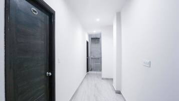 A hallway with a dark wooden door on the left, white walls, and a tiled floor.